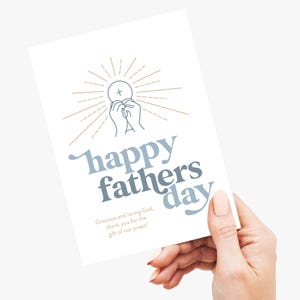 A hand holds a white greeting card with "happy fathers day" in blue and gray, and a communion host and hands graphic.