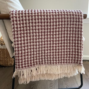 May include: A red and white checkered throw blanket with fringe on the bottom edge. The blanket is draped over a black metal stand.
