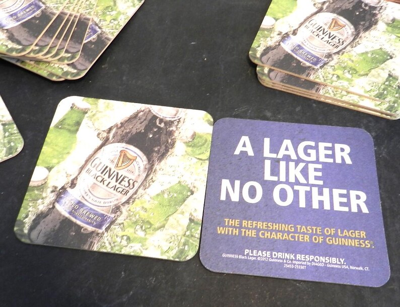 May include: Two square coasters featuring a bottle of Guinness Black Lager. One coaster has a photo of the bottle and the other has the text "A Lager Like No Other. The refreshing taste of lager with the character of Guinness."  Please drink responsibly.