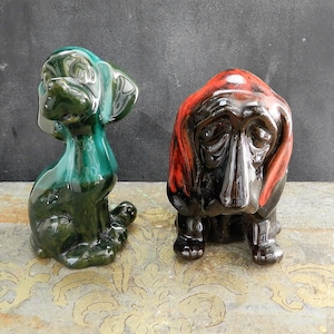 May include: Two ceramic dog figurines. One is green and the other is black with red accents.