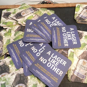 May include: A stack of blue and white square coasters with the text "A Lager Like No Other" and the words "The refreshing taste of lager with the character of Guinness."  Please drink responsibly.