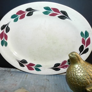 Puede incluir: Plato de servir ovalado de cerámica blanca con un diseño de hojas negras, verdes y rojas alrededor del borde.
