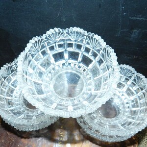 Könnte beinhalten: Eine Ansammlung von vier transparenten, geschliffenen Glasschalen. Jede Schale hat ein Diamantmuster und einen gewellten Rand. Die Schalen sind leicht überlappend angeordnet, was ihr kompliziertes Design und ihre Klarheit hervorhebt. Die Schalen sind wahrscheinlich zum Servieren.