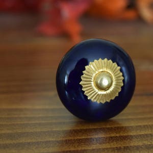 May include: A dark blue ceramic knob with a gold starburst design. The knob is round and has a smooth surface.