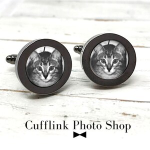 May include: A pair of black cufflinks with a round, silver-toned frame. Each cufflink features a black and white photo of a cat's face.