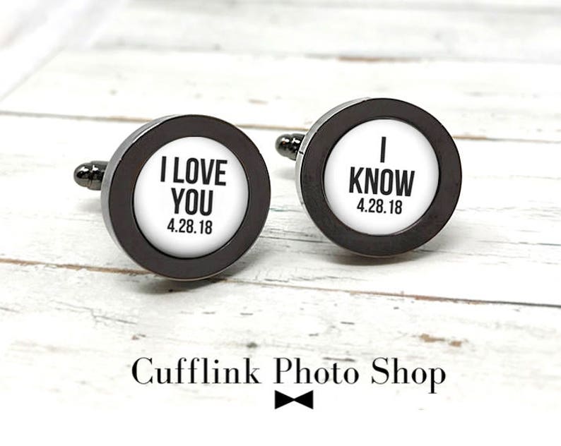 May include: A pair of silver cufflinks with black accents. One cufflink says "I Love You 4.28.18" and the other says "I Know 4.28.18".