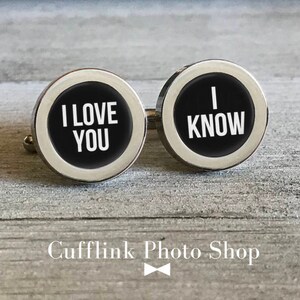 May include: A pair of silver cufflinks with black enamel. The left cufflink says "I love you" and the right cufflink says "I know".