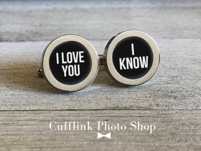 May include: A pair of silver cufflinks with black enamel. The left cufflink says "I love you" and the right cufflink says "I know".