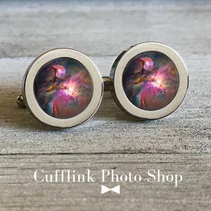 May include: A pair of silver cufflinks with a colorful nebula image inside. The cufflinks are round and have a polished finish.