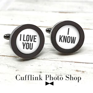 May include: A pair of black cufflinks with white circular inserts. One cufflink says "I LOVE YOU" and the other says "I KNOW".