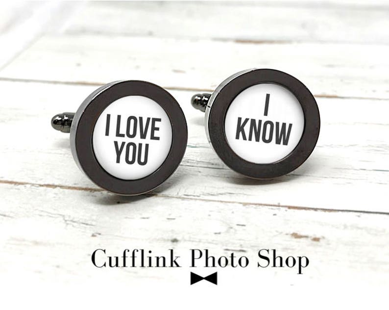 May include: A pair of black cufflinks with white circular inserts. One cufflink says "I LOVE YOU" and the other says "I KNOW".