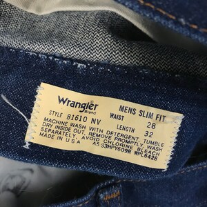 May include: A close-up of a blue denim Wrangler jeans label with white text. The label states "Style 81610 NV", "Mens Slim Fit", "Waist", "Length", "28", "32", "Machine Wash with Detergent, Tumble Dry Inside Out, Remove Promptly, Wash Separately, Avoid Chlorine Bleach", "Made in USA", "A5 S3HPY609R WPL6428".