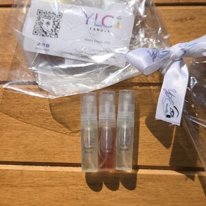May include: Three clear spray bottles with different colored liquids, labeled "Laundry Room", "Lavender Fields", and "Peachy Peach". The bottles are part of a gift set, with a white ribbon and a business card from YLC Candle.