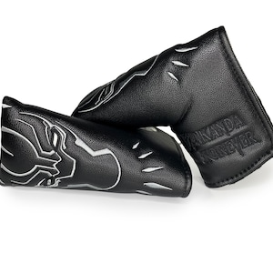 Puede incluir: Dos fundas para la cabeza de palo de golf negras. Una presenta una imagen bordada en plata de la cara de Black Panther. La otra tiene las palabras "Wakanda Forever" bordadas en plata.