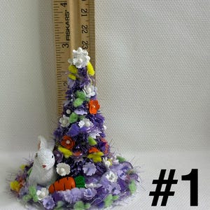 May include: A miniature Easter tree with a white bunny and carrot. The tree is decorated with purple, white, orange, and yellow flowers. The base is surrounded by a white lace trim. The number "1" is in black.