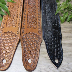 May include: Three leather guitar straps with intricate floral and woven patterns. The straps are brown, tan, and black.
