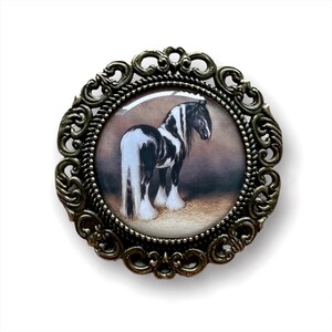 Peut inclure: Une image ronde encadrée représentant un cheval noir et blanc avec une crinière et une queue longues et flottantes. Le cadre est en métal orné de couleur dorée.