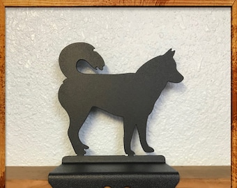 May include: Black metal stocking holder shaped like a dog with a paw print cutout. The holder is attached to a wooden surface.
