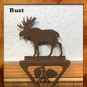 Peut inclure: Un porte-chaussettes en métal rouillé en forme d'élan avec un motif de pomme de pin. L'élan est debout sur une base triangulaire avec un motif de pomme de pin. Le porte-chaussettes est conçu pour accrocher des chaussettes sur une cheminée.