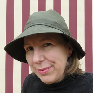 May include: A woman wearing a green, wide-brimmed hat with a black turtleneck sweater.