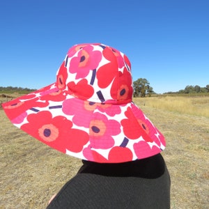 May include: A wide-brimmed sun hat with a floral print featuring large red and pink flowers on a white background. The hat has a black trim and a wide brim.