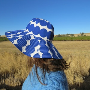 Könnte beinhalten: Ein blauer und weißer Sonnenhut mit großem Punkte-Muster. Der Hut ist aus Stoff und hat eine breite Krempe.