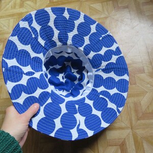 May include: A white and blue sun hat with a large brim and a blue polka dot pattern. The hat is made of a soft, textured fabric.