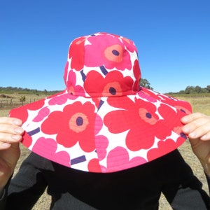 May include: A wide-brimmed sun hat with a red and white floral print. The hat has a large brim and a crown with a red flower design.