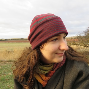 Può includere: Una donna indossa un berretto a righe grigie e rosse con un bordo ripiegato. Indossa anche una sciarpa multicolore e una giacca grigio scuro.