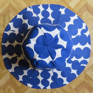May include: A white and blue sun hat with a large, white circle pattern and blue flower-shaped accents. The hat is made of fabric and has a wide brim.