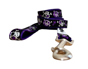 May include: Purple and black dog leash with silver skull and star pattern. The leash has a silver hook.