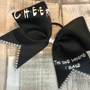 Könnte beinhalten: Schwarzer Cheer-Bogen mit weißem Text, der "CHEER" in der Schriftart von Friends und "THE ONE WHERE I BASE" auf der anderen Seite sagt. Der Bogen ist mit silbernen Strasssteinen verziert.