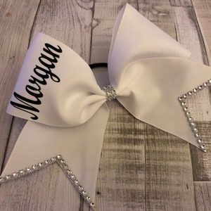 May include: White cheer bow with rhinestones and the name "Morgan" written in black.