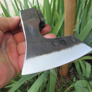 Puede incluir: Una mano sostiene un peque&ntilde;o hacha negra con una hoja plateada. El hacha tiene un mango de madera y una cabeza de metal. El hacha es afilada y tiene una ligera curva en la hoja.