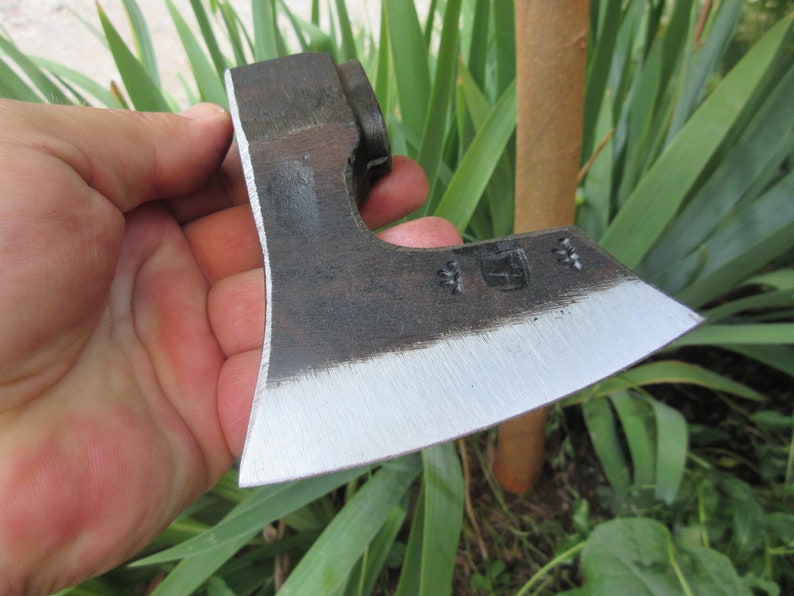 Puede incluir: Una mano sostiene un peque&ntilde;o hacha negra con una hoja plateada. El hacha tiene un mango de madera y una cabeza de metal. El hacha es afilada y tiene una ligera curva en la hoja.
