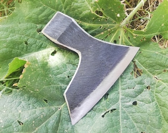 Peut inclure: Une hache en métal noir avec une lame tranchante et un manche en bois. La hache est posée sur une feuille verte avec des trous.