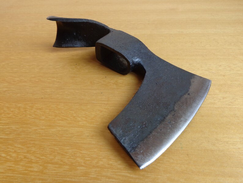 May include: A black metal hand axe with a curved blade and a wooden handle. The axe is on a wooden surface.