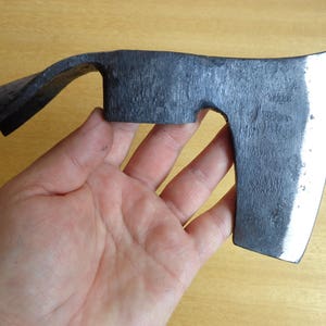 May include: A black hand axe with a curved handle and a slightly rounded blade. The axe has a polished finish and a slight bevel on the edge of the blade.