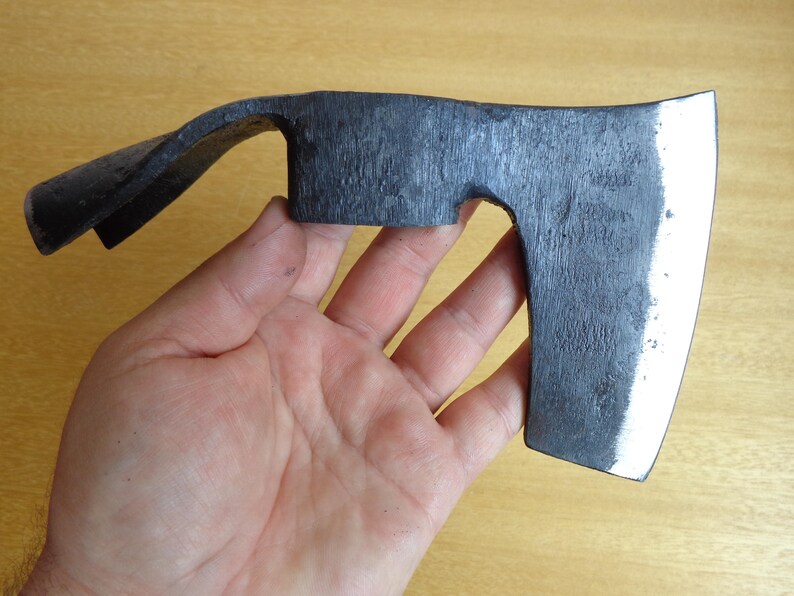 May include: A black hand axe with a curved handle and a slightly rounded blade. The axe has a polished finish and a slight bevel on the edge of the blade.