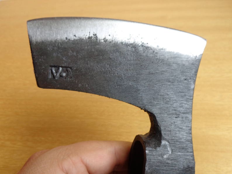 May include: A close-up of a gray metal axe head with a curved blade. The axe head has a small hole in the side and the text "12" is stamped on the side of the axe head.