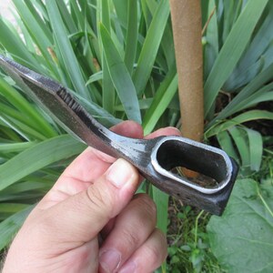 Puede incluir: Un peque&ntilde;o hacha curva forjada a mano con un mango negro. El hacha tiene una hoja afilada y un agujero en el mango para un cord&oacute;n.