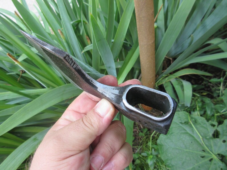 Puede incluir: Un peque&ntilde;o hacha curva forjada a mano con un mango negro. El hacha tiene una hoja afilada y un agujero en el mango para un cord&oacute;n.