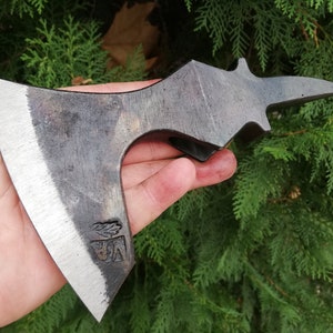 Könnte beinhalten: Eine Hand hält eine schwarze und silberne Axt mit einem Blattdesign auf der Klinge. Die Axt hat einen einzigartigen, gebogenen Griff.