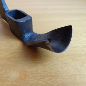 May include: A black metal hand adze with a curved blade and a wooden handle.