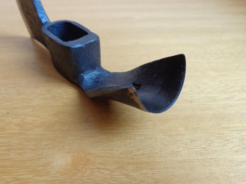 May include: A black metal hand adze with a curved blade and a wooden handle.