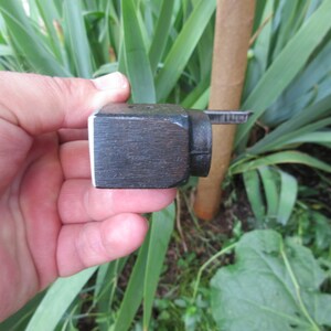 Puede incluir: Un peque&ntilde;o bloque de madera marr&oacute;n oscuro con un borde blanco. El bloque tiene una pieza de metal unida a &eacute;l, con un peque&ntilde;o tornillo de metal.