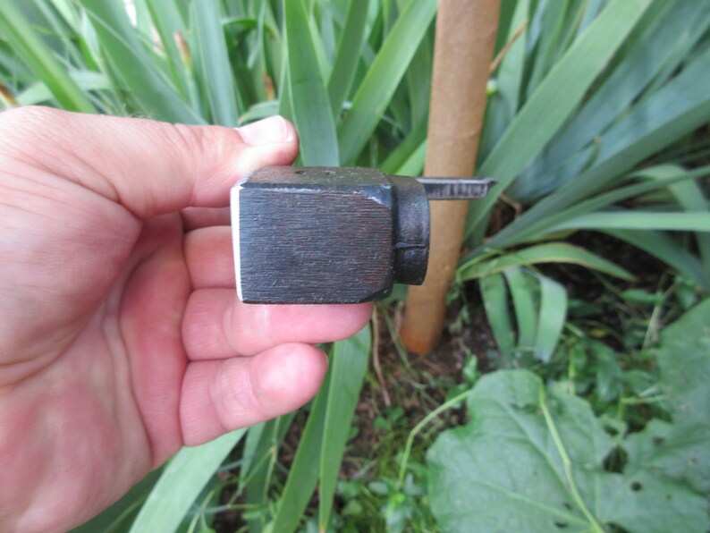Puede incluir: Un peque&ntilde;o bloque de madera marr&oacute;n oscuro con un borde blanco. El bloque tiene una pieza de metal unida a &eacute;l, con un peque&ntilde;o tornillo de metal.