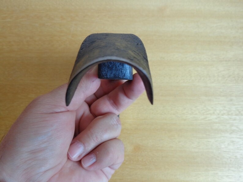 May include: A close-up of a dark brown leather strop with a black wooden handle. The strop is curved and is being held by a hand.