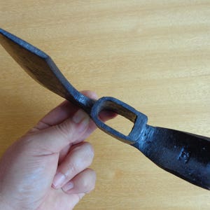May include: A black metal hand adze with a wooden handle. The adze has a sharp blade and a curved head.