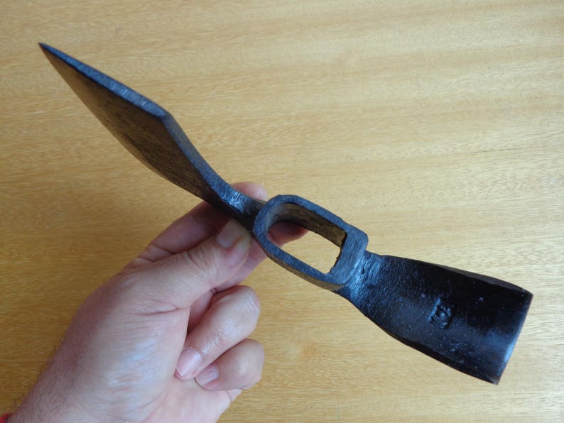 May include: A black metal hand adze with a wooden handle. The adze has a sharp blade and a curved head.